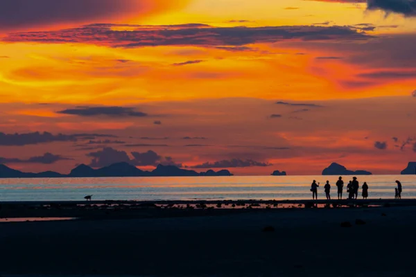 Saat akşam kum banka üzerinde dramatik alacakaranlık gökyüzü bulut üzerinde okyanus Adası ve A alan siluet insanlar yürümek