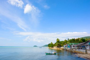 Küçük tekne demirlemiş deniz sahil plaj evleri önünde, açık mavi gökyüzü bulut güneşli gün doğal balıkçı köyü 