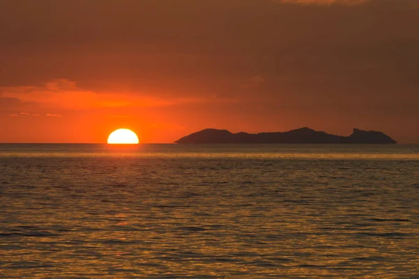 SUN GOING DOWN HIDDEN FROM HORIZON LINE NEARBY BIG ISLAND ,SCENIC LOOK OUT AT SEASIDE , LIGHT REFLECTING ON WATER , WONDERFUL TIME IN EVENING , GOLDEN DARK ORANGE TWILIGHT CLOUD BACKGROUND