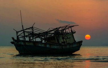 Siluet balıkçı tekne karaya düşük gelgit Denizi, su arka planda üzerinde günbatımı alacakaranlık gökyüzü üzerinde harap.