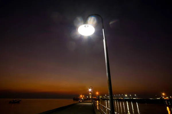 SEASIDE BRIDGE PIER AT NIGHT TWILIGHT DUSK SKY , ELECTRICAL LIGHTS REFLECTING ON WATER