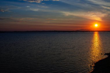 Mavi gökyüzü güneş doğuyor ve beyaz bulutlar gördüm çok uzak dağ gölge ağarma giden orada güneşin su yüzeyinde bir yansımasıdır.