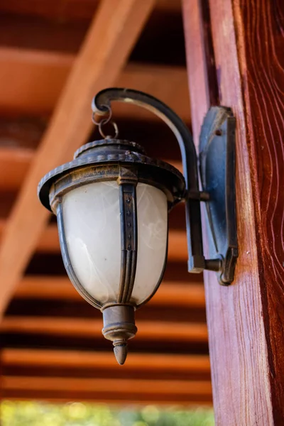 Lamba ayağı ile eski lamba direğine asılı lambalar beyaz cam ve kahverengi ahşap sütunlar ile süslenmiş.