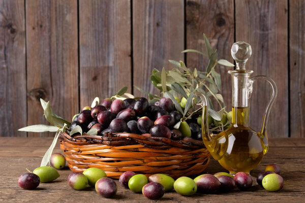 Olives in basket with bottle of oil on wooden table old