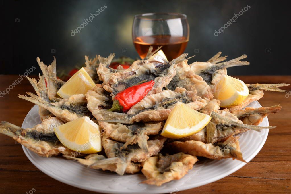 Sardinas empanadas y fritas en el plato con cuñas de limón y un chile 2023