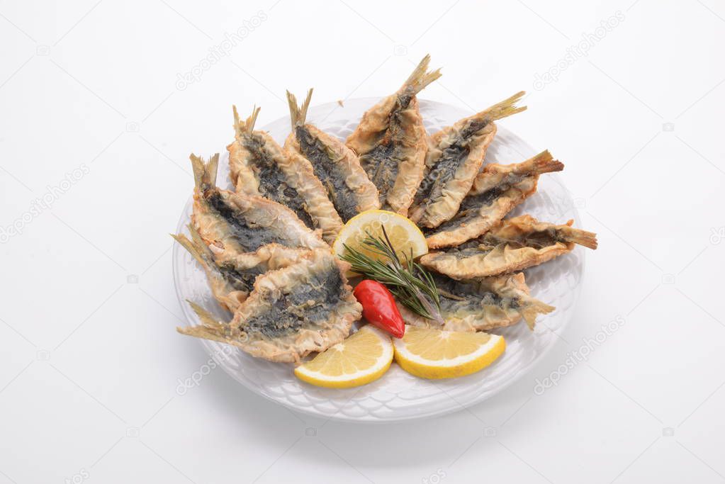 Sardines breaded and fried on plate with lemon wedges and a chili