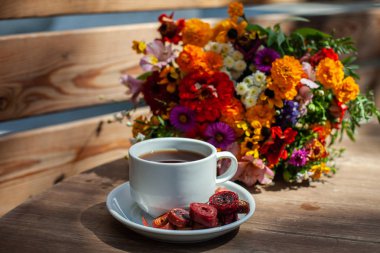 Ahşap bir masa üzerinde kır çiçekleri bir buket arka planda ev yapımı pastille ile kahve ile Beyaz kupa