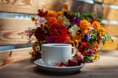 Ahşap bir masa üzerinde kır çiçekleri bir buket arka planda ev yapımı pastille ile kahve ile Beyaz kupa