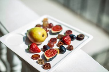 Deniz kıyısının arka planında meyve ve pastille içeren bir tabak. Nefis. Lüks.