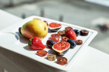 Deniz kıyısının arka planında meyve ve pastille içeren bir tabak. Nefis. Lüks.