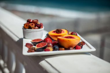 Deniz kıyısının arka planında meyve ve pastille içeren bir tabak. Nefis. Lüks.