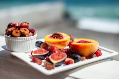 Deniz kıyısının arka planında meyve ve pastille içeren bir tabak. Nefis. Lüks.