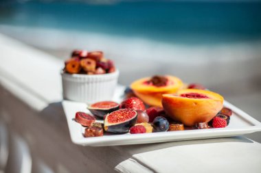 Deniz kıyısının arka planında meyve ve pastille içeren bir tabak. Nefis. Lüks.