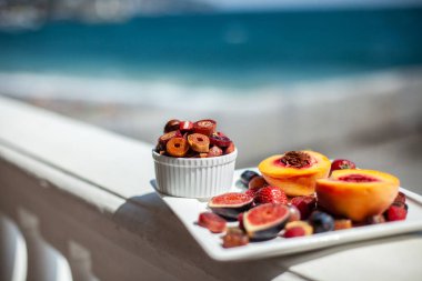 Deniz kıyısının arka planında meyve ve pastille içeren bir tabak. Nefis. Lüks.