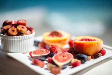 Deniz kıyısının arka planında meyve ve pastille içeren bir tabak. Nefis. Lüks.