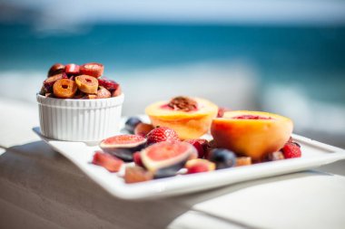 Deniz kıyısının arka planında meyve ve pastille içeren bir tabak. Nefis. Lüks.