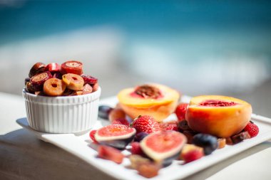 Deniz kıyısının arka planında meyve ve pastille içeren bir tabak. Nefis. Lüks.