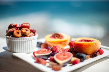 Deniz kıyısının arka planında meyve ve pastille içeren bir tabak. Nefis. Lüks.