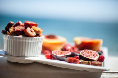 Deniz kıyısının arka planında meyve ve pastille içeren bir tabak. Nefis. Lüks.