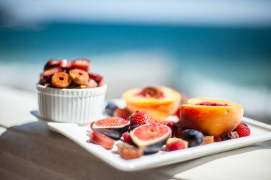Deniz kıyısının arka planında meyve ve pastille içeren bir tabak. Nefis. Lüks.