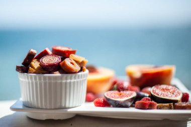 Deniz kıyısının arka planında meyve ve pastille içeren bir tabak. Nefis. Lüks.