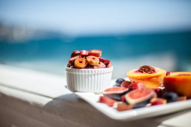 Deniz kıyısının arka planında meyve ve pastille içeren bir tabak. Nefis. Lüks.