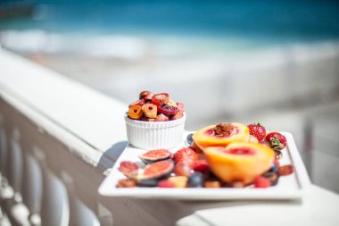 Deniz kıyısının arka planında meyve ve pastille içeren bir tabak. Nefis. Lüks.