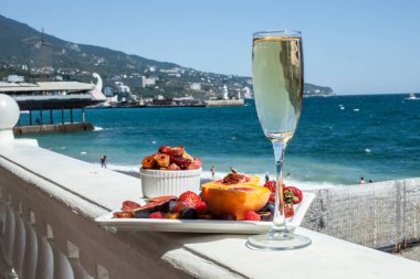 Deniz kıyısının arka planına karşı meyve ve şampanya içeren bir tabak. Nefis. Lüks.