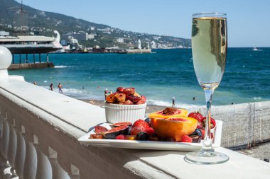 Deniz kıyısının arka planına karşı meyve ve şampanya içeren bir tabak. Nefis. Lüks.