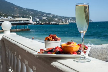 Deniz kıyısının arka planına karşı meyve ve şampanya içeren bir tabak. Nefis. Lüks.