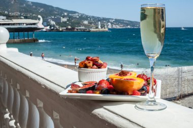 Deniz kıyısının arka planına karşı meyve ve şampanya içeren bir tabak. Nefis. Lüks.