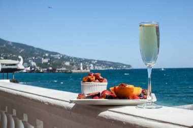 Deniz kıyısının arka planına karşı meyve ve şampanya içeren bir tabak. Nefis. Lüks.