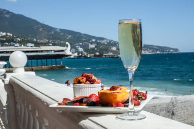 Deniz kıyısının arka planına karşı meyve ve şampanya içeren bir tabak. Nefis. Lüks.