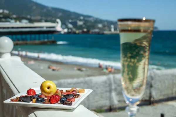 A dish with fruit and champagne against the background of the sea shore. Yummy. Luxuriously.