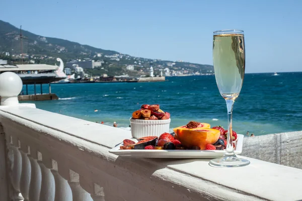 Deniz kıyısının arka planına karşı meyve ve şampanya içeren bir tabak. Nefis. Lüks.