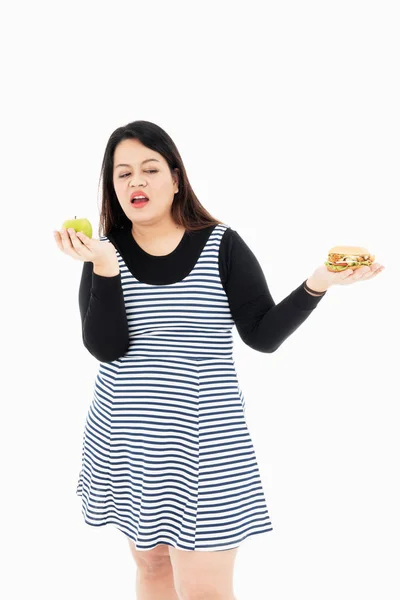 Uma jovem gorda escolhe uma maçã ou um hambúrguer . — Fotografia de Stock