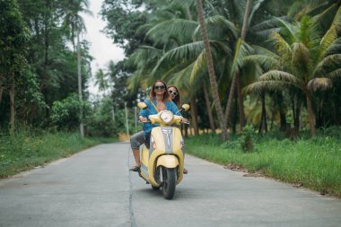 Bir çift güzel kadınların seyahat tarafından scooter Güneydoğu Asya'da ormanın içinden. Tayland