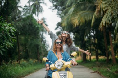 Bir çift güzel kadınların seyahat tarafından scooter Güneydoğu Asya'da ormanın içinden. Tayland