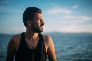 Genç bir adam gün batımında deniz görünüyor. Yakışıklı bir adam gün batımında denize buzlu oturuyor. Portre