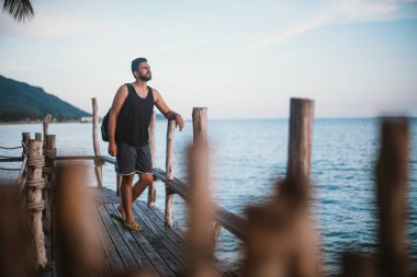 Genç bir adam bir ahşap köprü üzerinde günbatımında okyanusta yürür. Yakışıklı adam okyanusun Güneydoğu Asya'da tarafından gün batımını izlemek