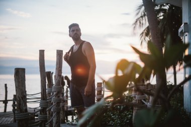 Genç bir adam bir ahşap köprü üzerinde günbatımında okyanusta yürür. Yakışıklı adam okyanusun Güneydoğu Asya'da tarafından gün batımını izlemek