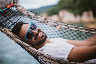 Okyanus tarafından bir hamakta yatan genç adam. Yakışıklı olan bir denizin kenarında dağların fon karşı bir hamakta dinleniyor.