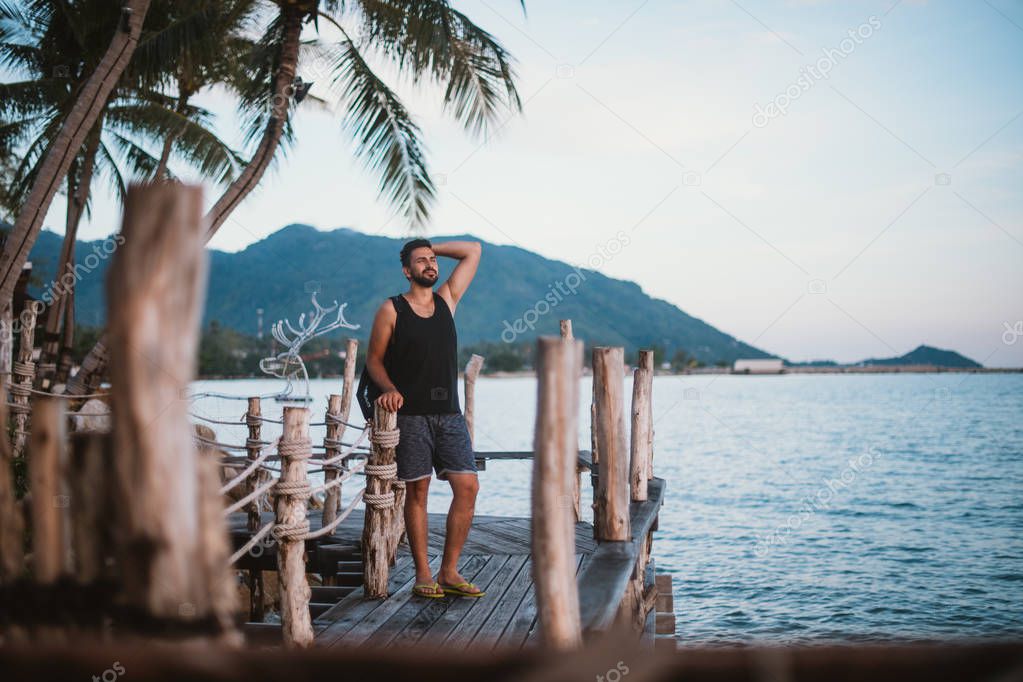 A young guy walks on a wooden bridge at sunset on the ocean. Handsome man watching sunset by the ocean in Southeast Asia