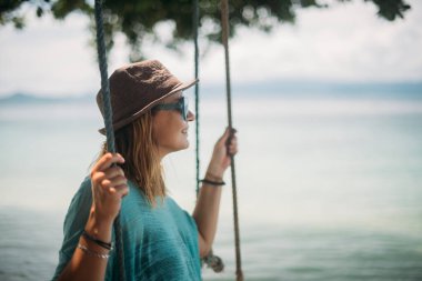 Genç bir kadın deniz kenarında büyük bir ağaç gölgesinde bir salıncak üzerinde sallanıyor. Kız bir tropik ada'nın kıyısındaki beach salıncak üzerinde.