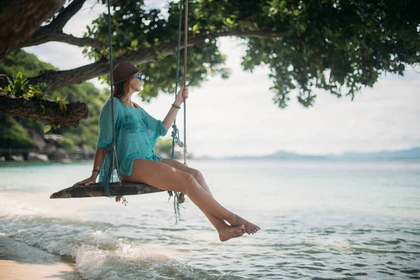若い女性が海のそばの大きな木の陰にあるブランコに揺れています 熱帯の島の海岸にビーチ スイングの少女 — ストック写真