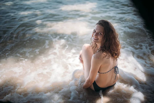 熱帯の島の海岸に海の波のように木の陰に座っている若いスリムな女の子 — ストック写真