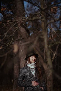 Genç bir kadın, güneşli bir günde sonbahar Ormanda yürür. Bir kız bir palto ve şapka ağaçların dallarında portresi