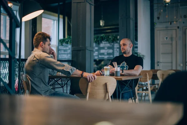 两个年轻人在一杯咖啡旁在咖啡馆里交流 男人们在一家小餐馆的桌子上说得很活泼 很积极 — 图库照片