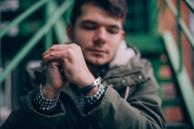 Endüstriyel bir manzara içinde genç bir adam portresi. Adam düşünceli metal merdivenlerinde oturur