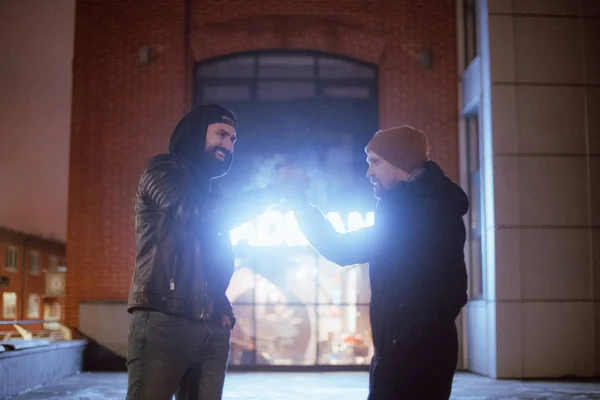 Two young men greet hand. Greeting two friends by the arm in a frosty evening on a dark street.